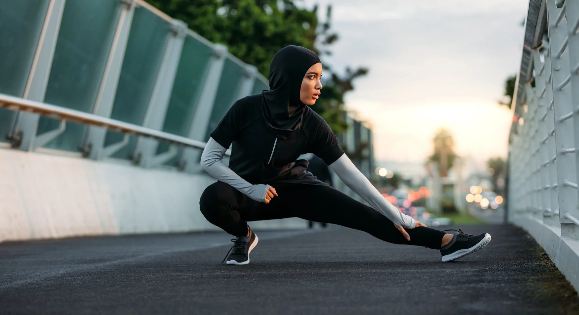Una mujer con ropa deportiva estira en una pasarela al amanecer