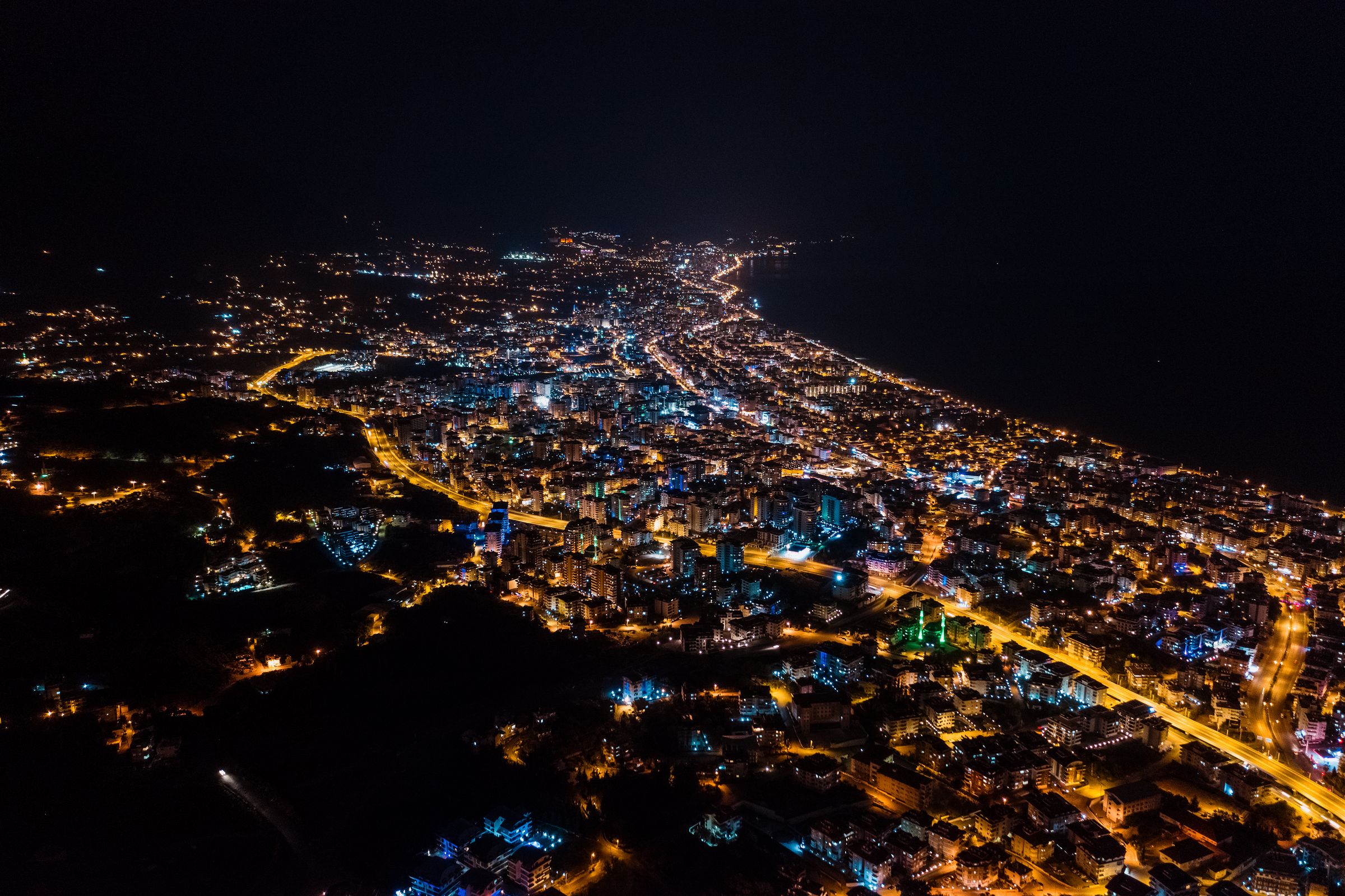 Vista aérea nocturna de una ciudad junto al mar, con las calles iluminadas