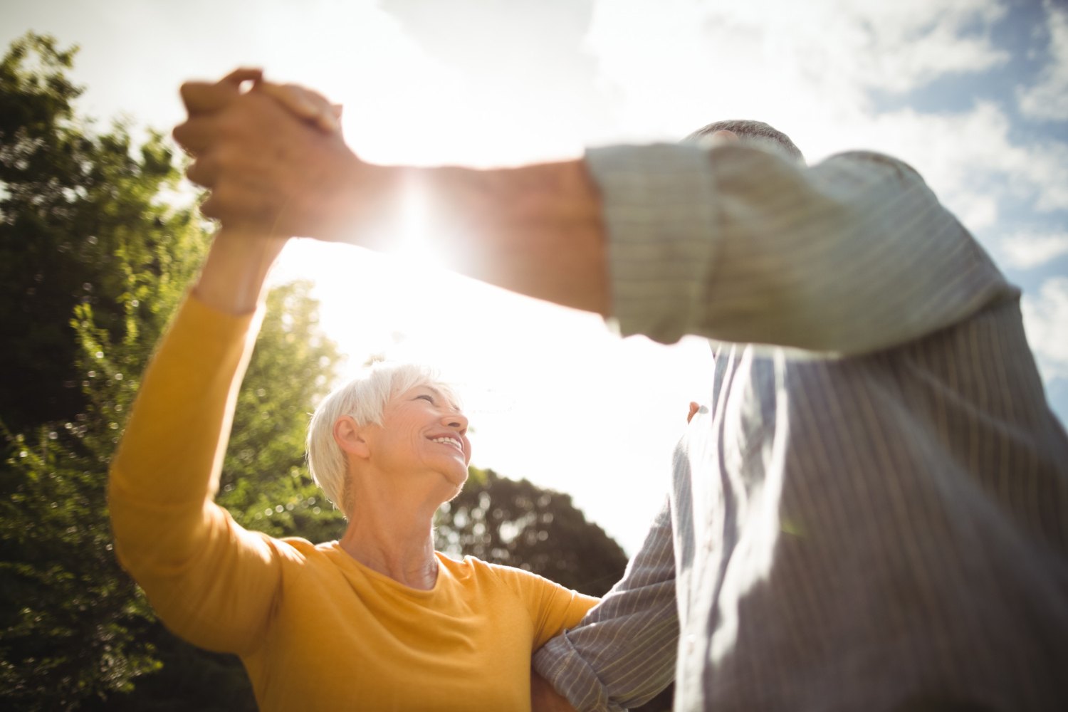 Una pareja de personas mayores baila al sol en un parque, cogidos de la mano